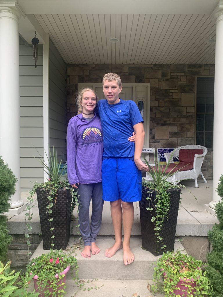 Abram boy in blue and Maci girl in purple stand in front of house for a first day of school picture